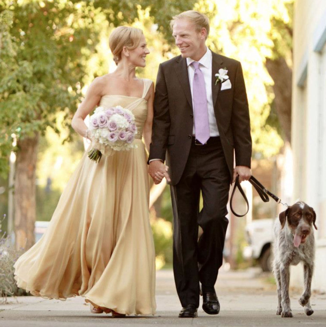 A bride in a custom gold silk gown walking with her groom